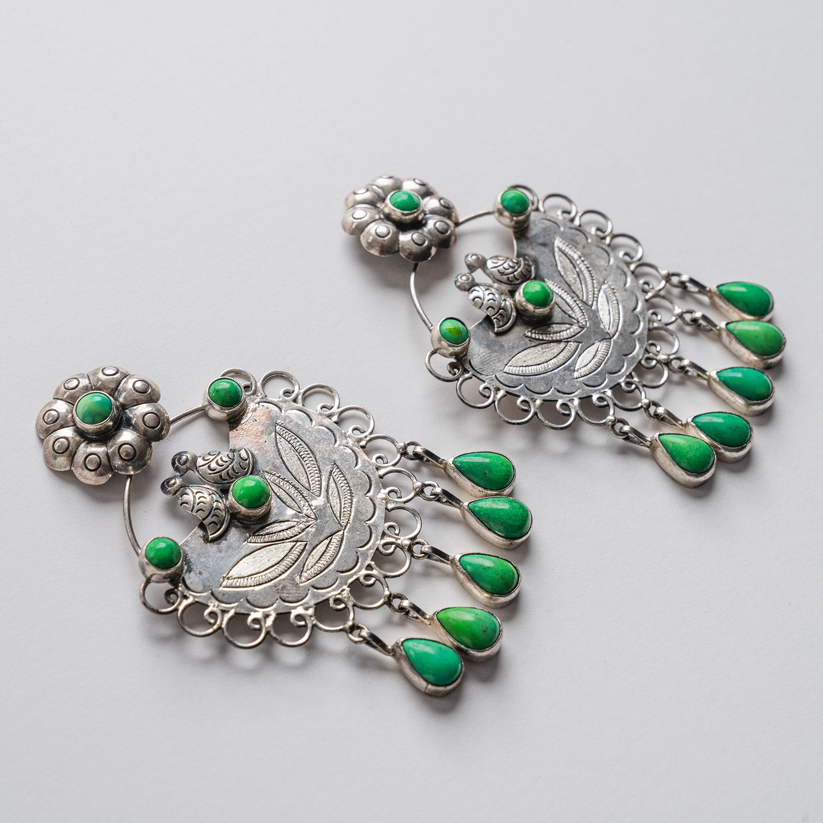 A pair of silver-toned dangle earrings with green turquoise stone accents and teardrop charms.
