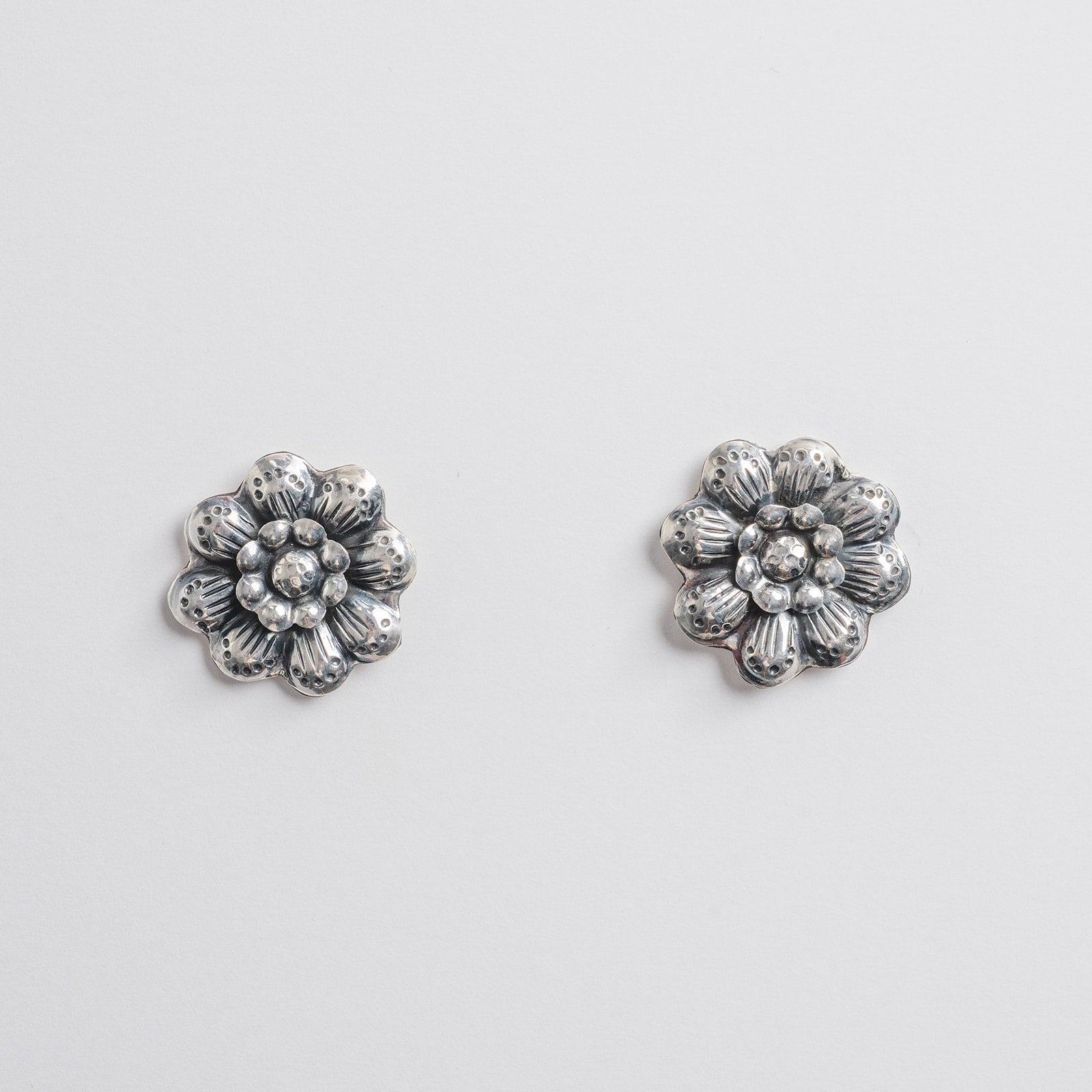 A pair of silver-toned flower-shaped stud earrings with stamped textured petals and  center.