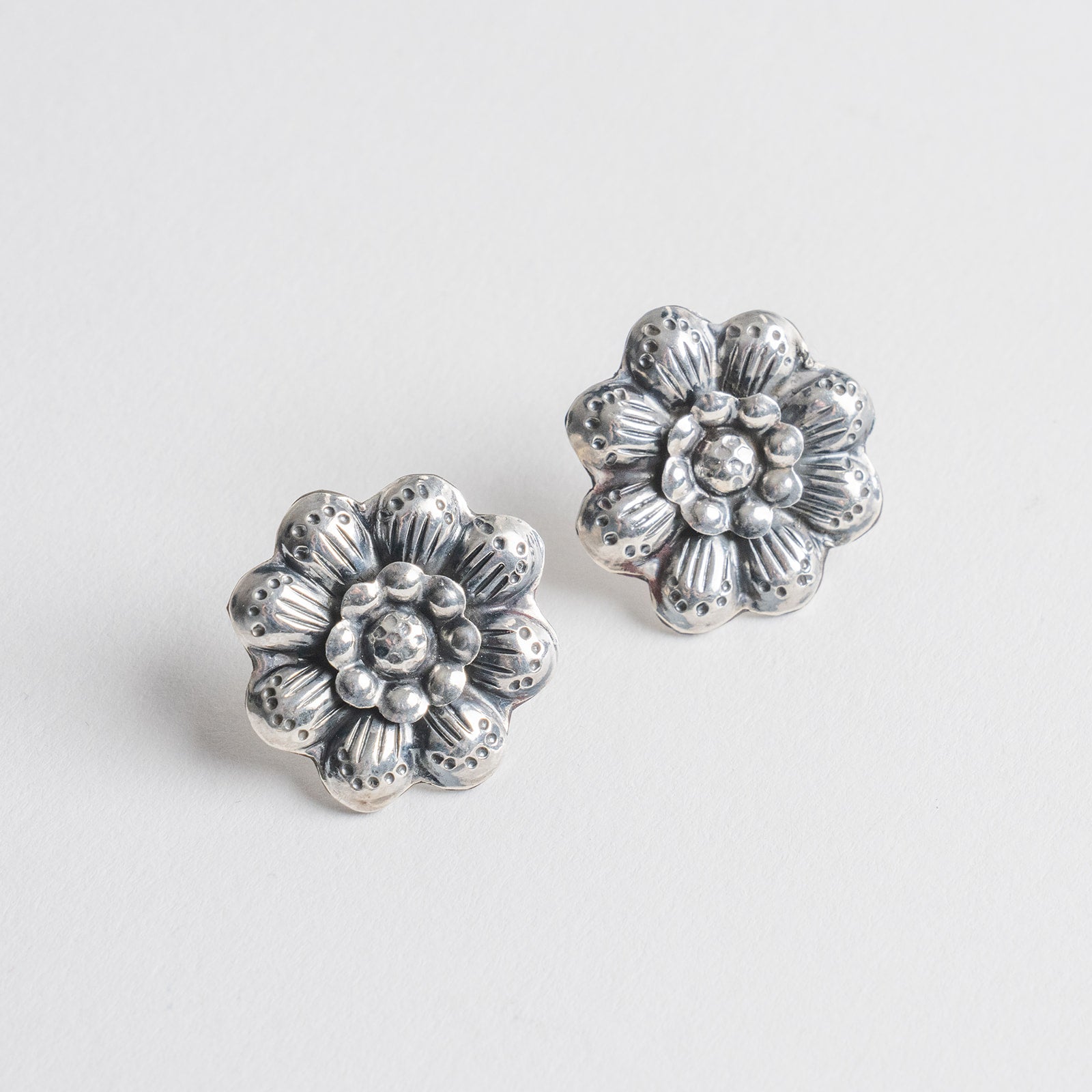 A pair of silver-toned flower-shaped stud earrings with stamped textured petals and  center.