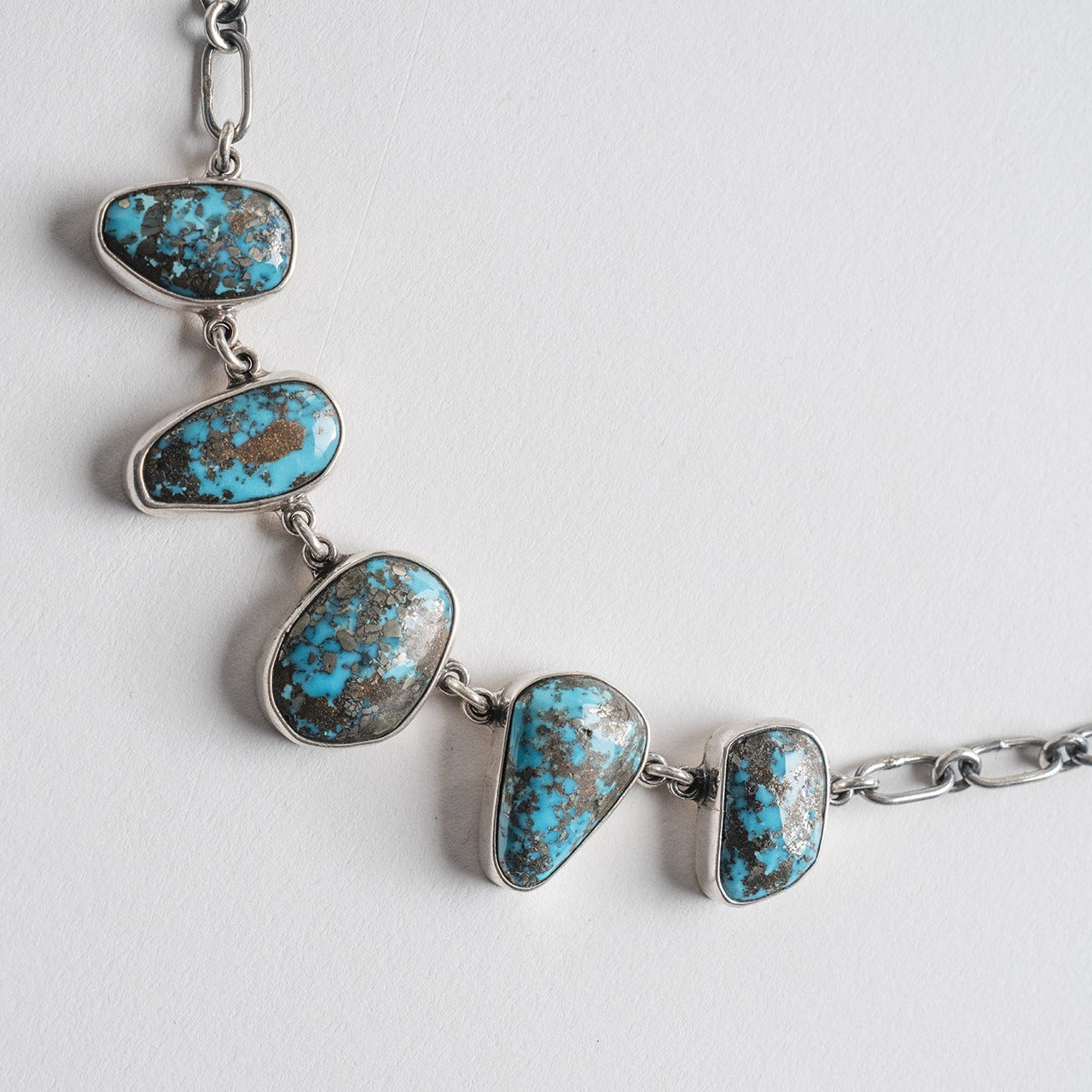 A silver-toned chain necklace featuring five irregular, turquoise-blue stones with dark matrix inlay, arranged in a row at the center.